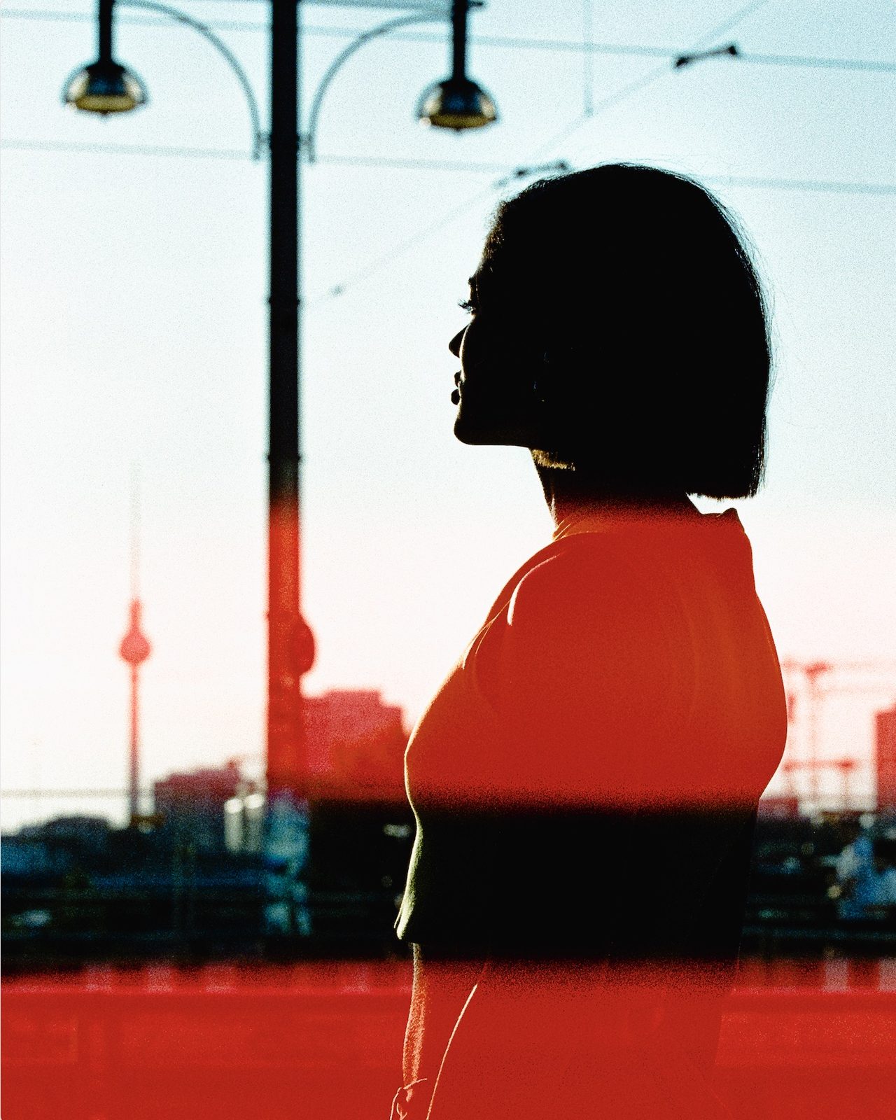 Analogue film portrait of a woman gazing towards the Berlin TV Tower, with light leaks from CineStill 800T film. Noirnor by Alex Sokolov, Woman Portrait Gallery.