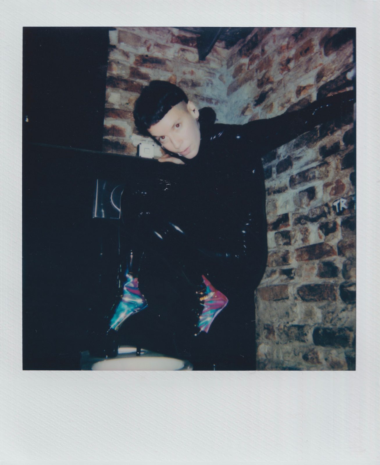 Polaroid snapshot from Berlin nightlife, a young woman possibly a DJ in front of a brick wall in a club with a typical Berlin bowl cut. Super Sonia by Altea Federico, Woman Portrait Gallery.